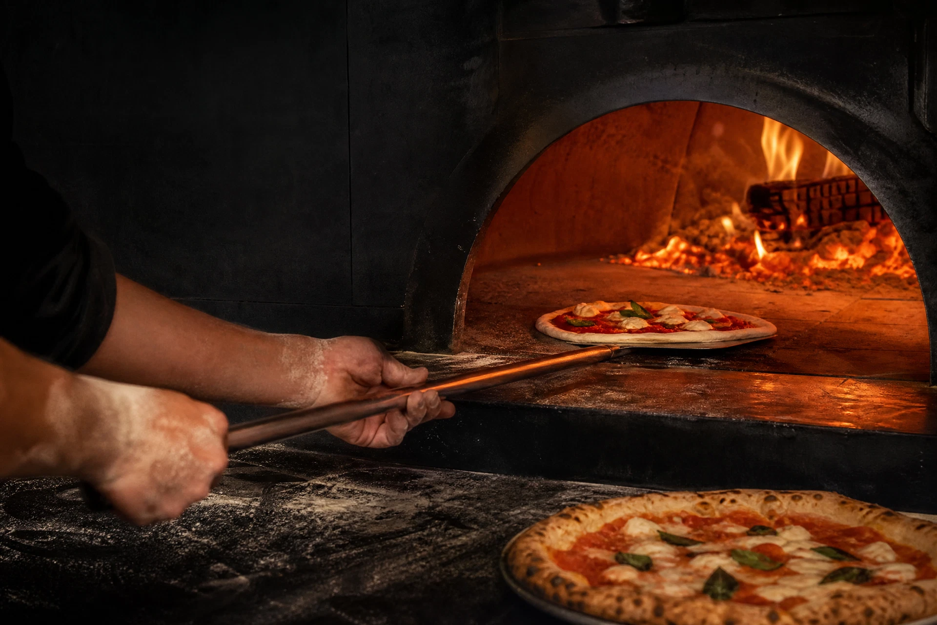 Pizza being loaded into a wood-fired oven